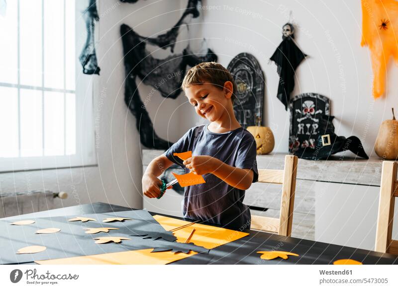 Smiling little boy cutting out for Halloween decoration at home decorating decorations All Hallows' Eve boys males smiling smile celebration Red-Letter Day