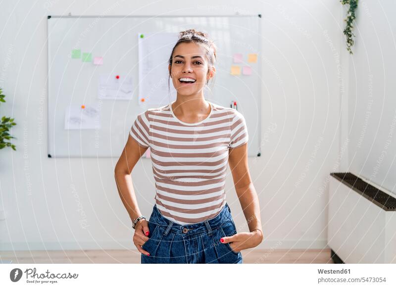 Happy beautiful female architect standing with hands in pockets against whiteboard at workplace color image colour image indoors indoor shot indoor shots
