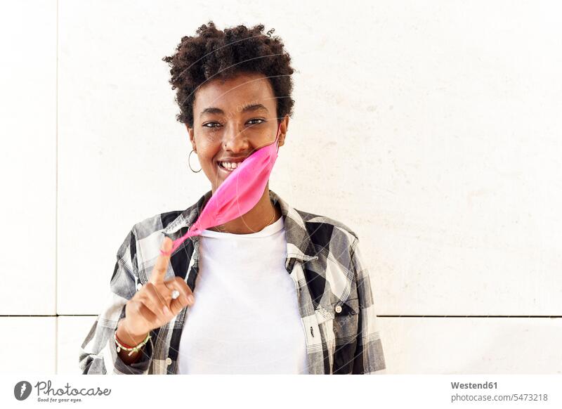 Smiling young woman removing pink mask against white wall color image colour image Spain outdoors location shots outdoor shot outdoor shots day daylight shot