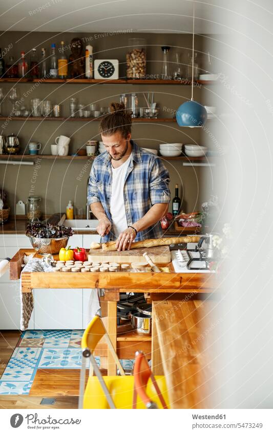 Young man preparing food at home, slicing bread cooking Food Preparation young man young men kitchen domestic kitchen kitchens Baguette Baguettes French stick