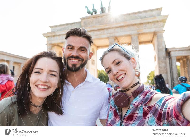 Portrait of three happy friends taking selfie with cell phone in front of Brandenburger Tor, Berlin, Germany touristic tourists cell phones Cellphone mobile