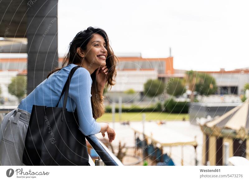 Smiling woman with purse leaning on railing in city color image colour image outdoors location shots outdoor shot outdoor shots day daylight shot daylight shots