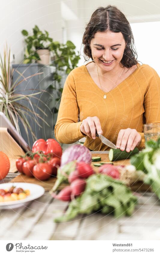 Young woman cutting cucumber while standing by table at home color image colour image indoors indoor shot indoor shots interior interior view Interiors day