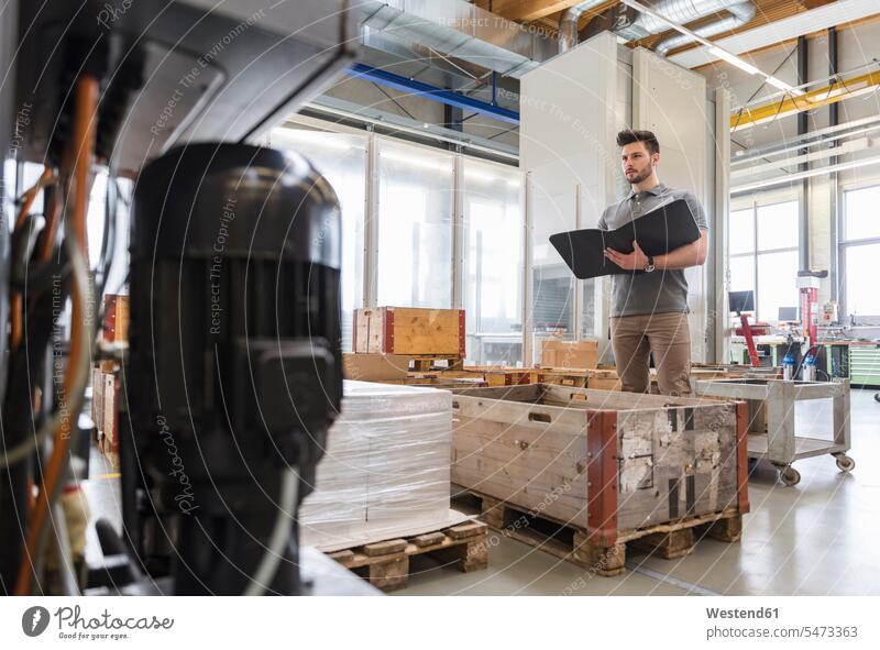 Man with folder standing in factory storeroom factories man men males file folders portfolio portfolios files storage room stockroom Adults grown-ups grownups