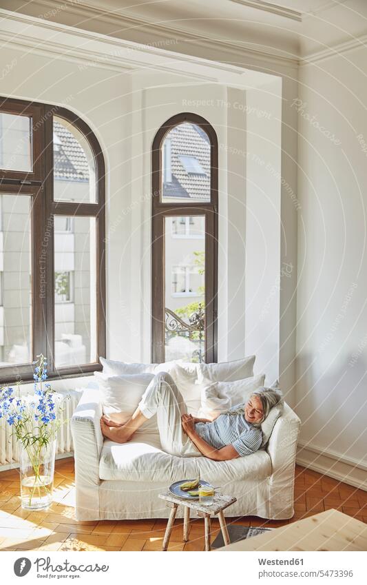 Smiling woman looking at food while lying on sofa in living room Germany indoors indoor shot indoor shots interior interior view Interiors day daylight shot