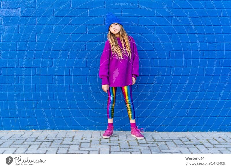 Portrait of girl wearing blue cap and oversized pink pullover standing in front of blue wall sweater jumper Sweaters fashionable head cocked blue background