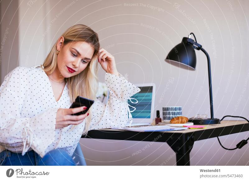 Blond businesswoman sitting at desk, working office offices office room office rooms businesswomen business woman business women blond blond hair blonde hair