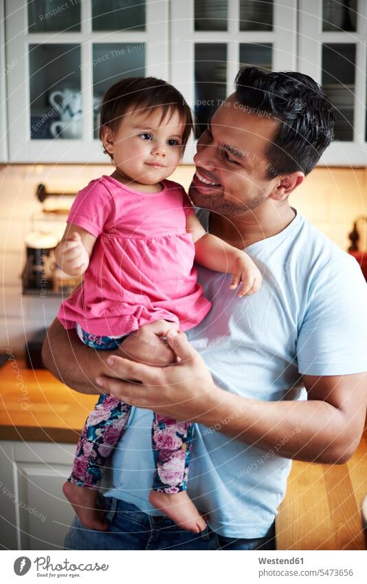 Smiling father holding baby girl in kitchen at home smiling smile daughter daughters pa fathers daddy dads papa infants nurselings babies child children family