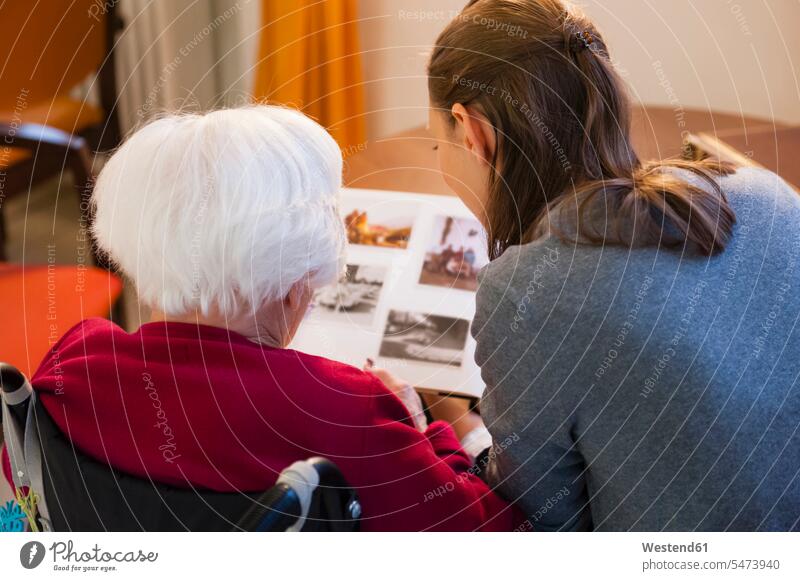 Grandmother with granddaughter looking photo album at home color image colour image Germany indoors indoor shot indoor shots interior interior view Interiors