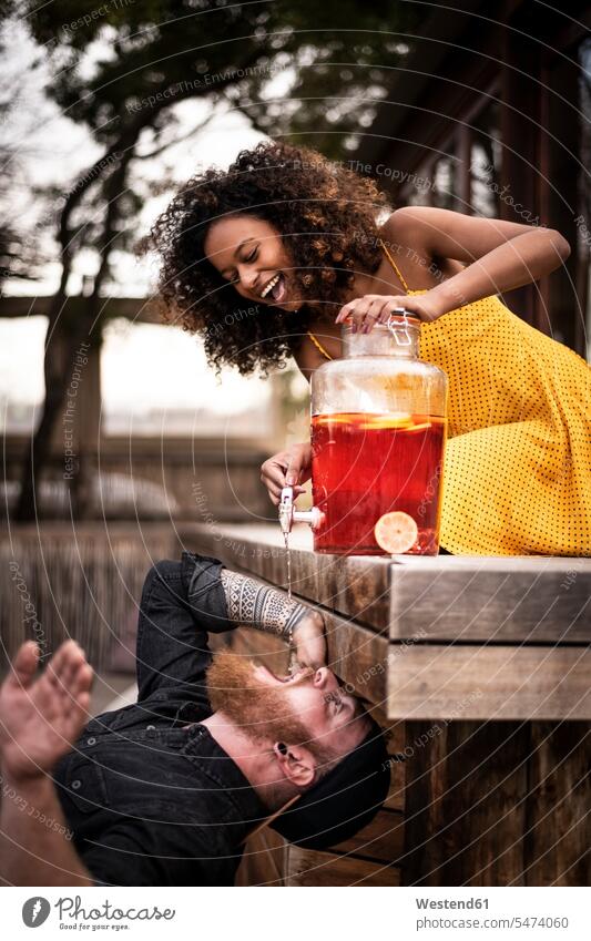 Happy woman pouring ice tea into boyfriend's mouth touristic tourists human human being human beings humans person persons curl curled curls curly hair drink