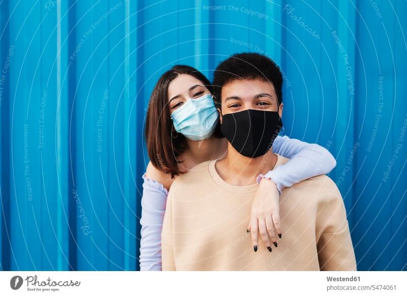Young woman with arm around on boyfriend while standing against blue wall during Covid-19 color image colour image outdoors location shots outdoor shot