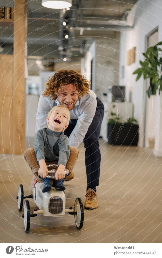 Businessman pushing son on toy car in office Occupation Work job jobs profession professional occupation business life business world business person