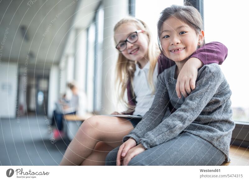 Portrait of two smiling schoolgirls sitting on school corridor hallway corridors hallways portrait portraits schools female pupils School Girl School Girls