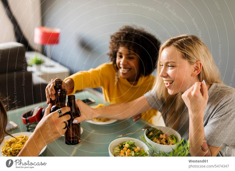 Happy girlfriends sitting at dining table clinking beer bottles Girlfriends girl friend girl friends Beer Beers Ale toasting cheers happiness happy Seated
