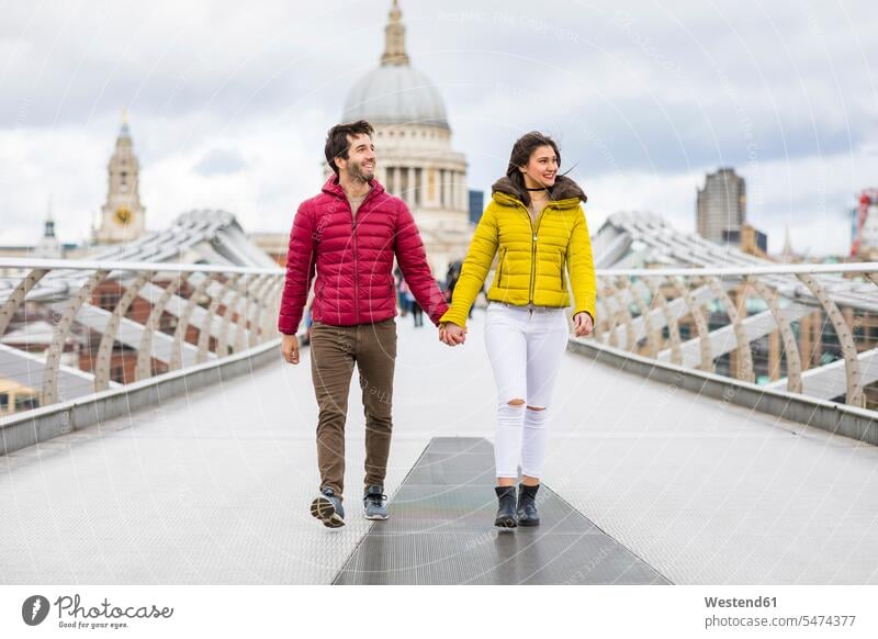 UK, London, young couple walking hand in hand on bridge in front of St Pauls Cathedral going bridges twosomes partnership couples cathedral cathedrals people