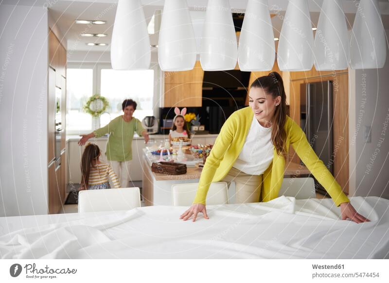 Smiling woman spreading the tablecloth at home with family in background smiling smile families laying the table laying table setting the table lay the table