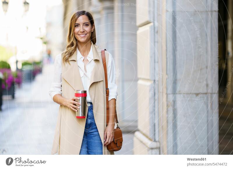 Beautiful woman with purse and metal thermos standing at sidewalk in city color image colour image outdoors location shots outdoor shot outdoor shots day