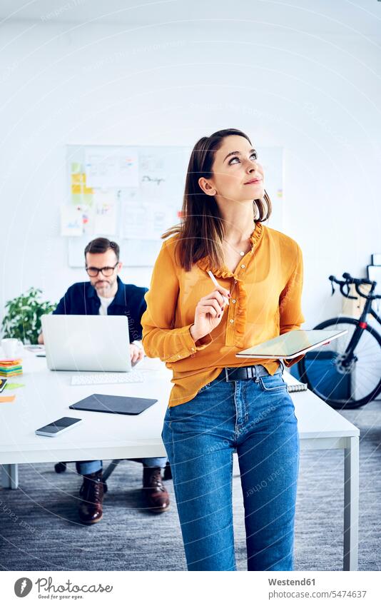 Businesswoman holding tablet in office with colleague in background offices office room office rooms colleagues digitizer Tablet Computer Tablet PC