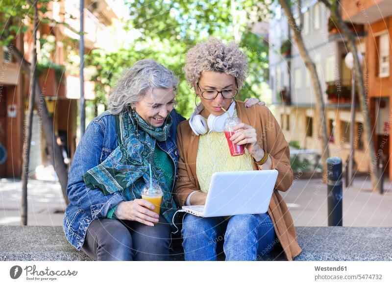 Senior mother with her adult daughter using laptop and drinking juices in the city human human being human beings humans person persons caucasian appearance