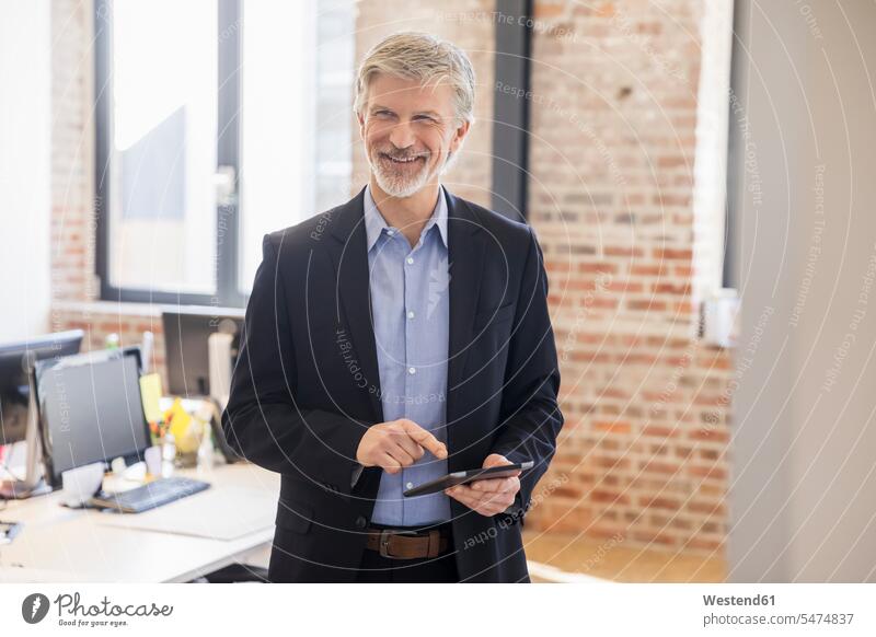 Mature man standing in his office, using didgital tablet offices office room office rooms Businessman Business man Businessmen Business men digitizer