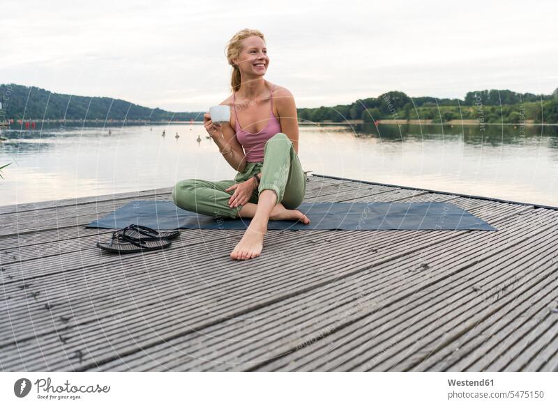 Young woman drinking coffee from cup at a lake towels relax relaxing hold smile Seated sit in the morning summer time summertime summery relaxation delight