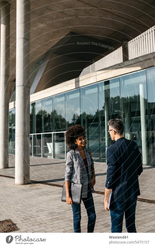 Two colleagues talking outside office building office buildings speaking built structure built structures face to face Facing Each Other looking at each other