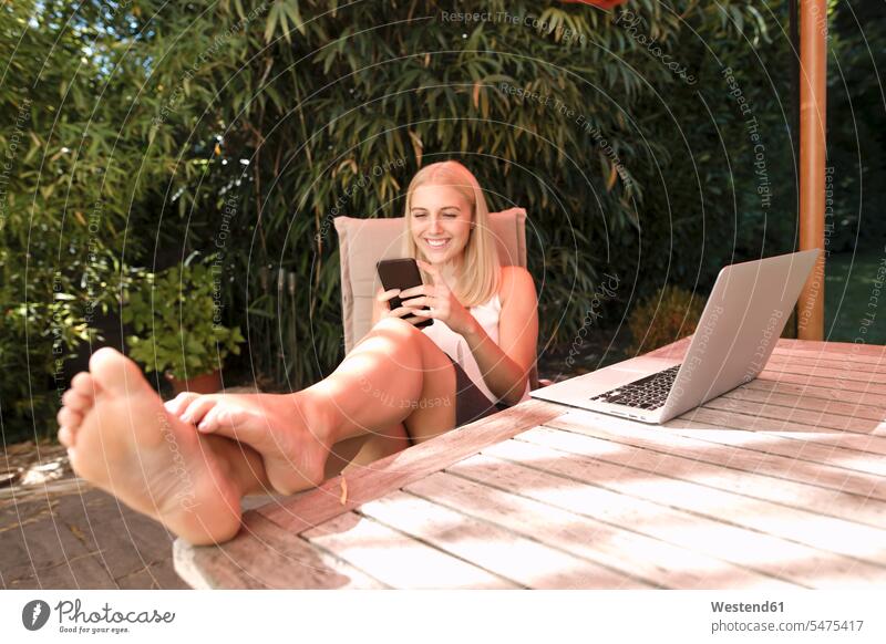 Young woman using smartphone in garden sitting Seated laughing Laughter gardens domestic garden Smartphone iPhone Smartphones on the phone call telephoning