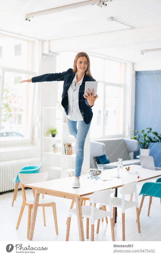 Young businesswoman balancing on one leg on desk in the board room, holding digital tablet Pretending To Fly Pretending to be a plane digitizer Tablet Computer