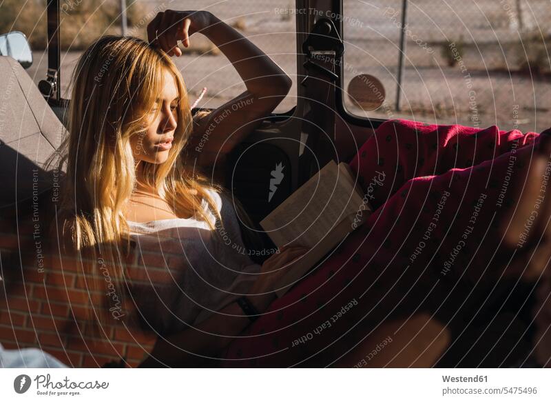 Young woman sitting in a car reading book Seated automobile Auto cars motorcars Automobiles books females women motor vehicle road vehicle road vehicles