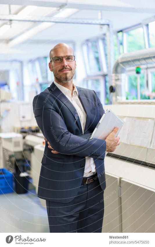 Confident male professional holding digital tablet while standing with arms crossed by machinery at illuminated factory color image colour image indoors