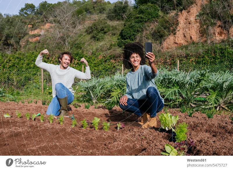 Couple taking selfies of planting lettuce seedlings in an vegetable garden rural country countryside organic flexing muscles Field Fields farmland Selfie