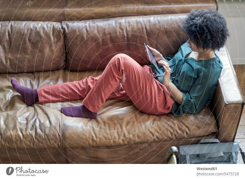 Young woman lying on couch using tablet females women laying down lie lying down settee sofa sofas couches settees digitizer Tablet Computer Tablet PC