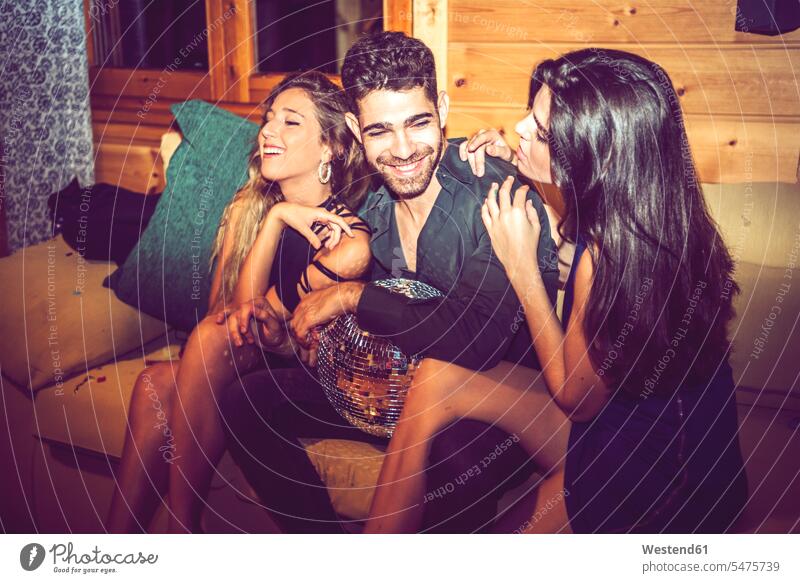 Young women flirting with man while sitting with him on sofa in party - a  Royalty Free Stock Photo from Photocase