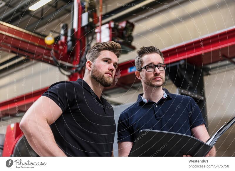 Two men with folder on factory shop floor looking around production hall colleagues factories looking round look round look around file folders portfolio