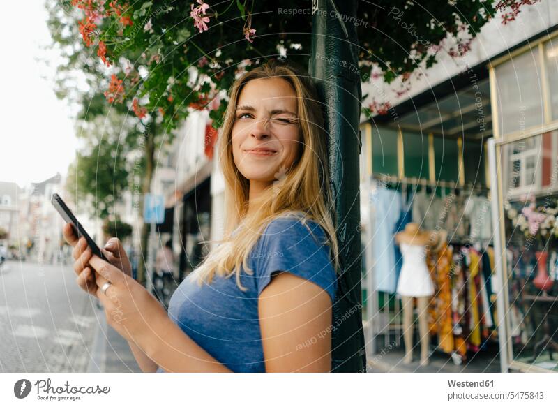 Netherlands, Maastricht, smiling young woman with cell phone in the city twinkling twinkle blinking mobile phone mobiles mobile phones Cellphone cell phones