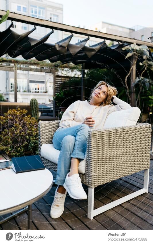 Thoughtful woman looking up with hand in hair sitting on chair at rooftop garden color image colour image outdoors location shots outdoor shot outdoor shots day