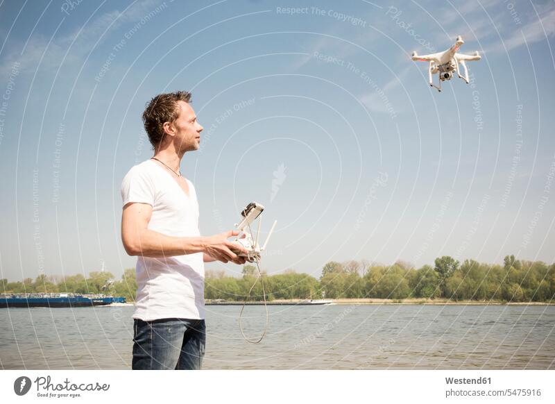 Man flying drone at a river drones River Rivers man men males water waters body of water Adults grown-ups grownups adult people persons human being humans
