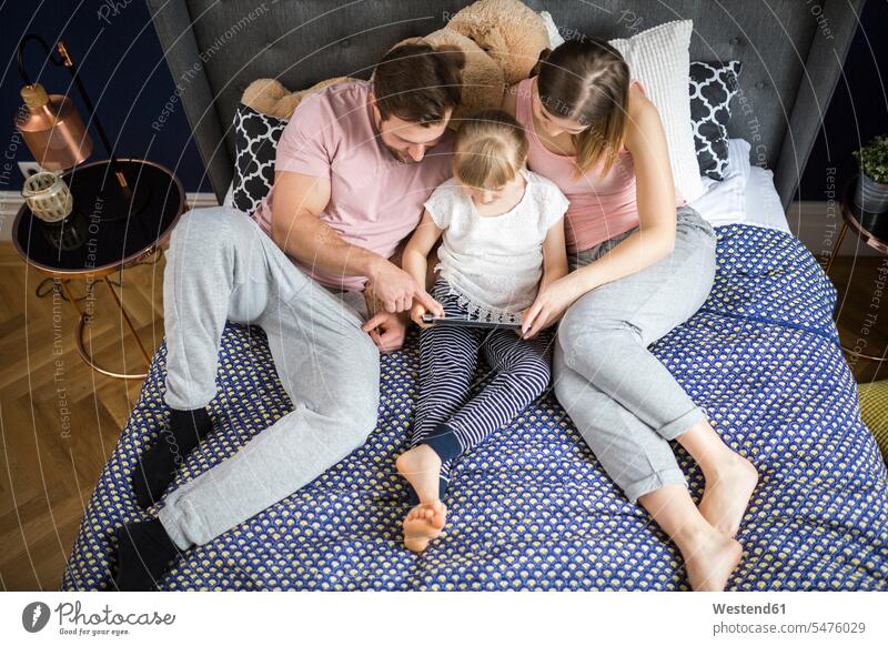 happy family sitting on bed, watching something on digital tablet with little daughter daughters families digitizer Tablet Computer Tablet PC Tablet Computers