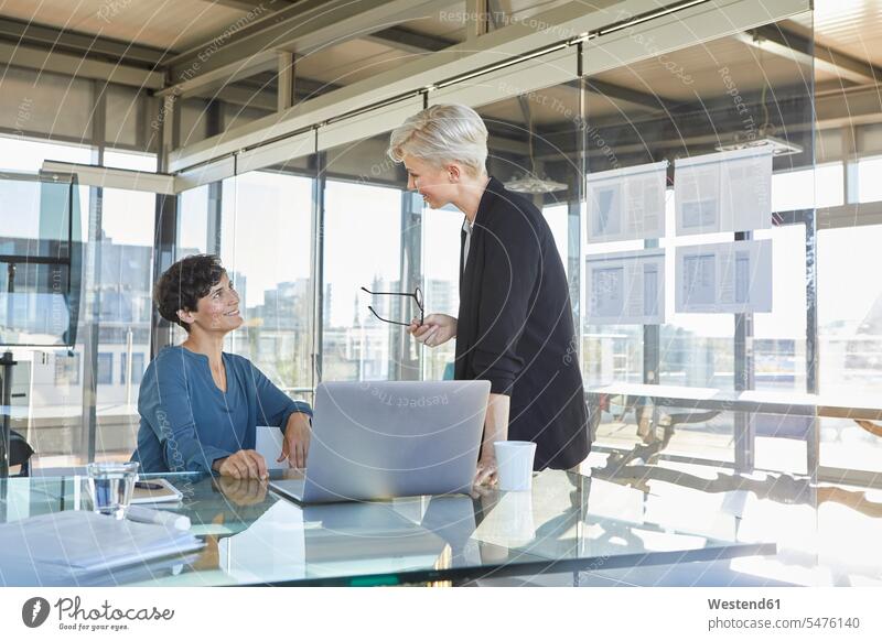 Two smiling businesswomen discussing at desk in office discussion businesswoman business woman business women smile offices office room office rooms desks