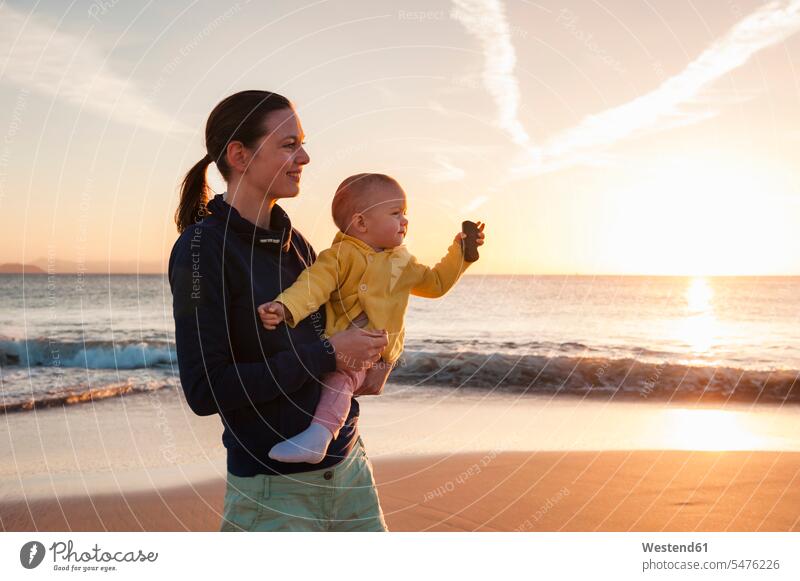 Mother holding little daughter on the beach at sunset beaches sunsets sundown mother mommy mothers ma mummy mama daughters baby infants nurselings babies