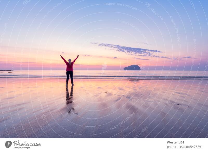 Mature woman with arms raised standing at Seacliff Beach during sunset, North Berwick, Scotland color image colour image sunsets sundown atmosphere Idyllic