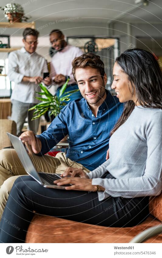 Smiling businessman and businesswoman using laptop on sofa in loft office Laptop Computers laptops notebook couch settee sofas couches settees Business Meeting