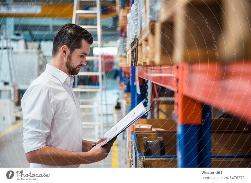 Man in factory storehouse holding folder storage room stockroom storeroom man men males factories file folders portfolio portfolios files dumps Adults grown-ups