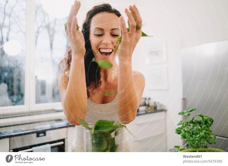 Fit woman standing in kitchen, preparing healthy smoothie, putting ingredients into blender human human being human beings humans person persons