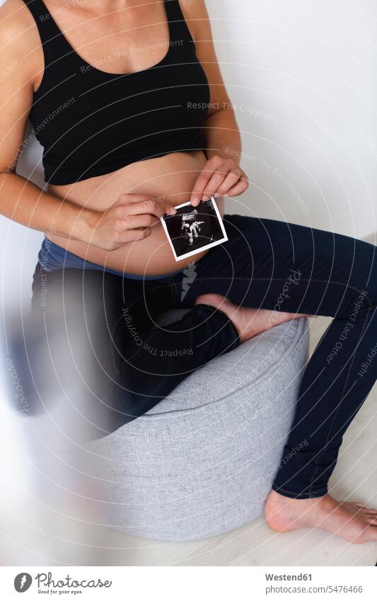 Young pregnant woman with ultrasound image of her unborn baby upper part of the body bellies stomach stomachs hold Seated sit happy Contented Emotion pleased