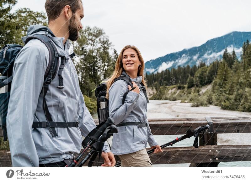 Young couple on a hiking trip walking on wooden bridge, Vorderriss, Bavaria, Germany touristic tourists back-pack back-packs backpacks rucksack rucksacks go