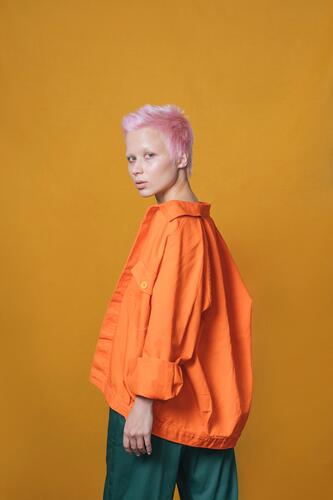 Portrait of young woman with short pink hair wearing orange jacket in front of yellow background human human being human beings humans person persons punks coat