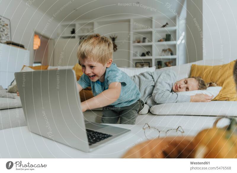 Boy using laptop by mother sleeping on sofa at home color image colour image indoors indoor shot indoor shots interior interior view Interiors day daylight shot