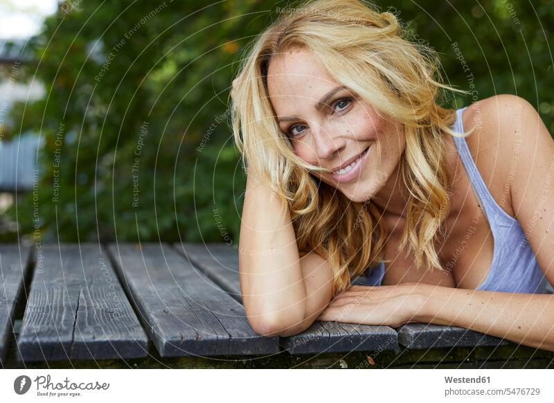 Portrait of smiling blond woman lying on wooden jetty portrait portraits laying down lie lying down jetties females women smile blond hair blonde hair Adults