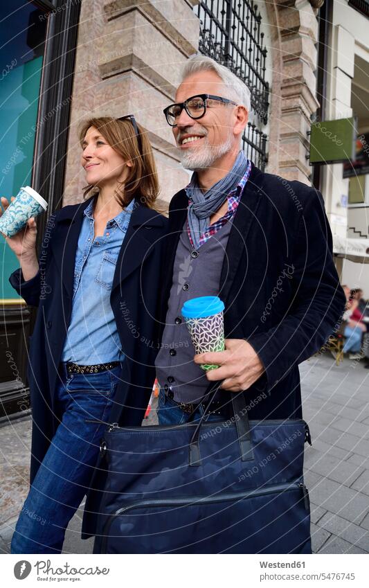 Smiling mature couple with reusable bamboo cups walking in the city Munich glasses specs Eye Glasses spectacles Eyeglasses beard Germany fashionable tourist
